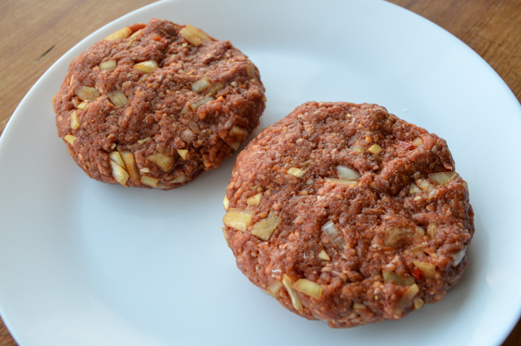 Two raw beef patties with onions, our uncooked Balkan burgers, on a white plate