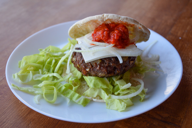 A Balkan burger, our version of pljeskavica inspired by cevapi, on a plate surrounded by green cabbage