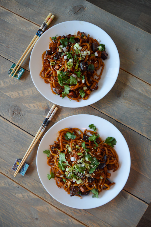 Two plates of udon noodles with miso roasted eggplants and chopsticks on a table