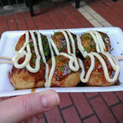 A hand holding a tray of 6 takoyaki balls in Tokyo