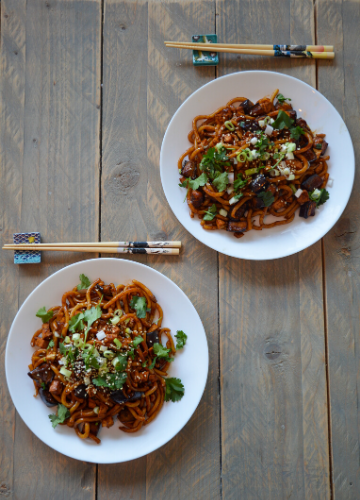 Two plates of udon noodles with miso roasted eggplant and chopsticks on a table