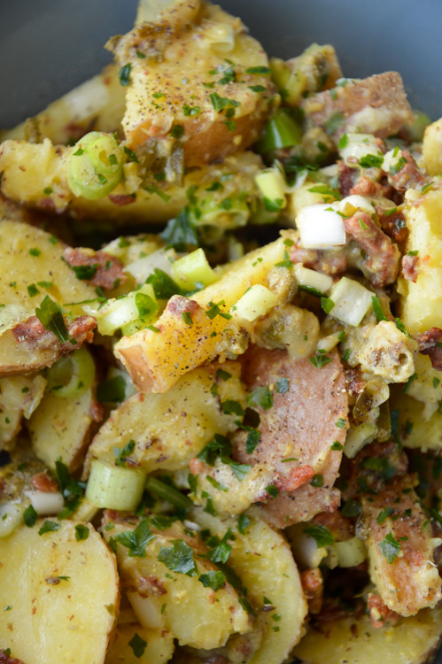 Close-up of potato salad where you can see green onions, parsley, bacon, and black pepper