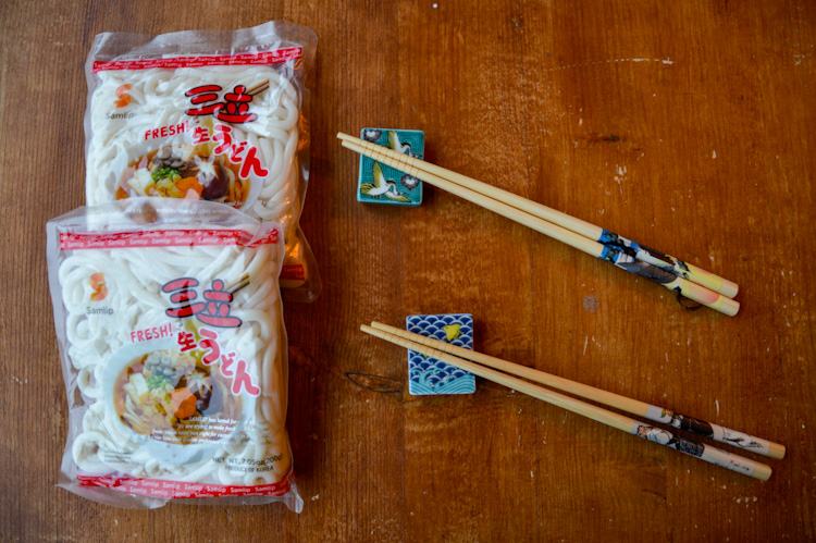 Two packages of udon noodles on a table next to two sets of chopsticks