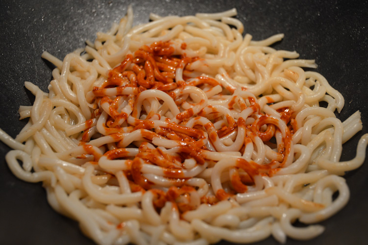 Udon noodles in a wok covered in peanut butter sauce