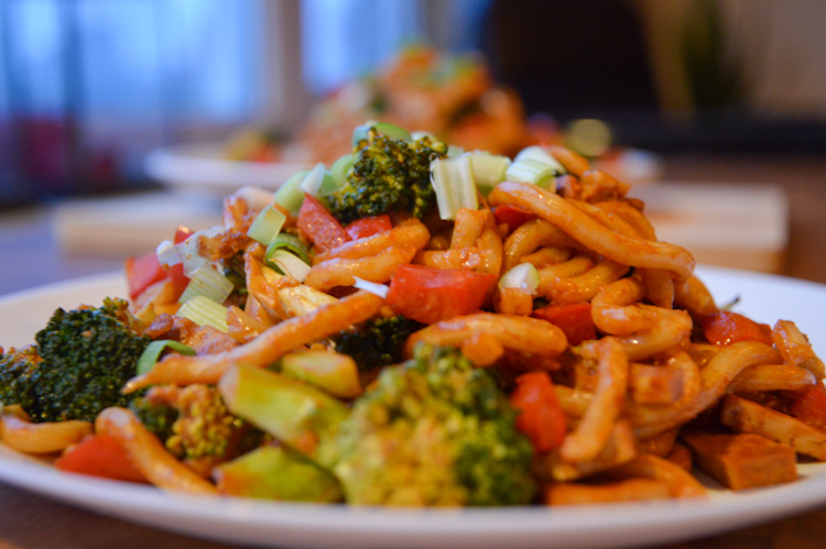 Close up of a plate of veggie udon noodles with broccoli and red pepper