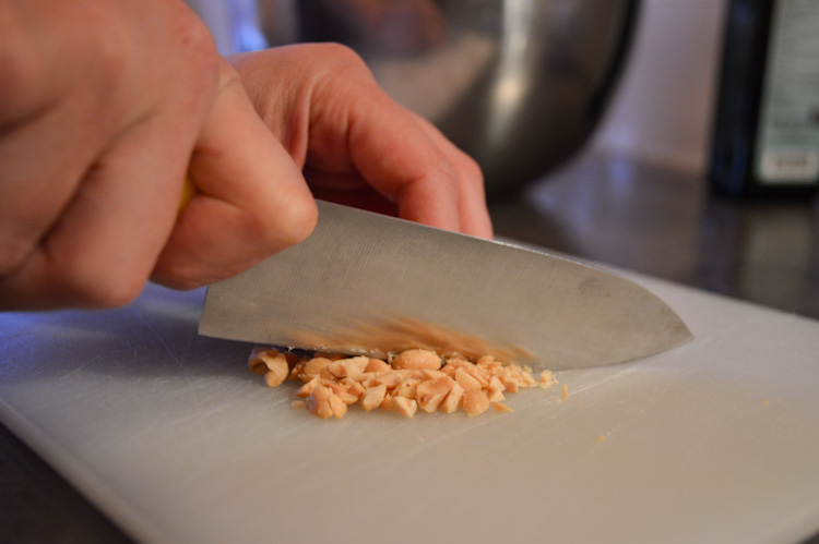 Hands chopping peanuts with a knife on a cutting board for Dutch peanut sauce