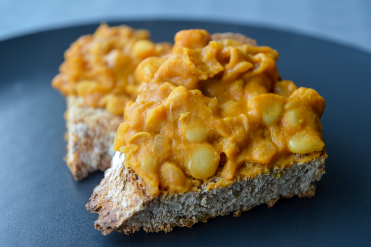 Macedonian beans (our version of tavce gravce made with canned beans) atop two pieces of crusty toast on a black plate