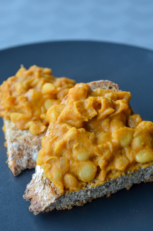 Orange colored mashed beans - our take on tavce gravce - on top of toasted crusty bread on a black plate