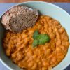 Light green bowl with deep orange tavce gravce inspired Macedonian beans with a piece of toasted bread