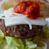 Super close up our Balkan burger showing toppings of feta cheese, raw onion, and ajvar