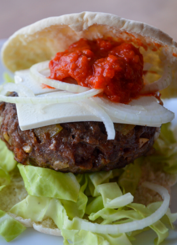 Super close up our Balkan burger showing toppings of feta cheese, raw onion, and ajvar