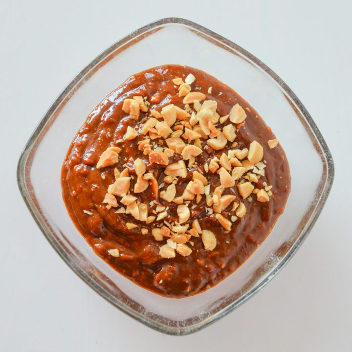 Glass bowl of pindasaus (Dutch peanut sauce) topped with chopped peanuts