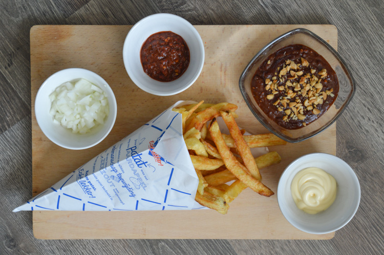 All the ingredients for patatje oorlog (Dutch war fries): fries, pindasaus, mayonnaise, raw onions, and sambal