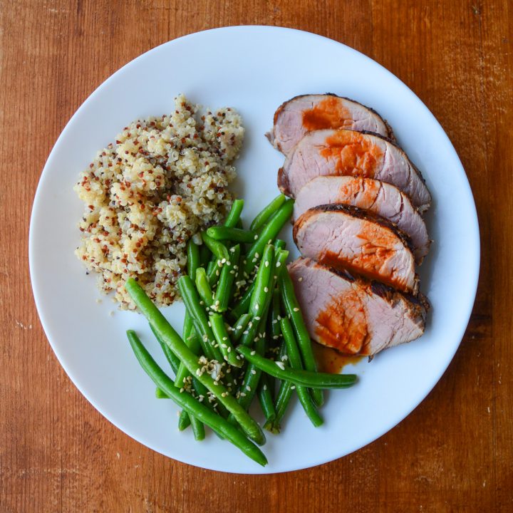 Thai grilled pork tenderloin sliced and sauced, on a plate with quinoa and green beans