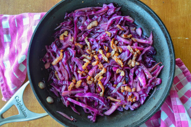 A skillet with sautéed red cabbage with bacon set on a pink and white towel
