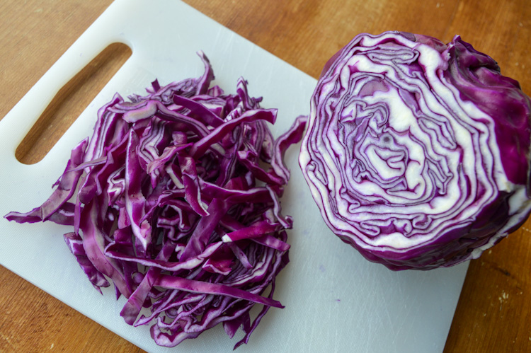 Half a red cabbage and half a cabbage chopped on a white cutting board