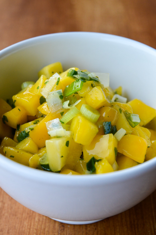 Close up of a white bowl of spicy mango salsa with a brown table background