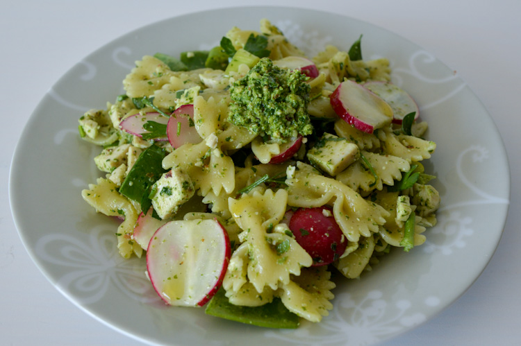 An angled view of a plate of radish greens pesto pasta salad with sliced radishes