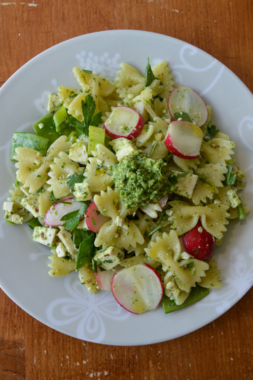 Plate of pesto greens pasta salad with chicken and sliced radishes sitting on a wooden table