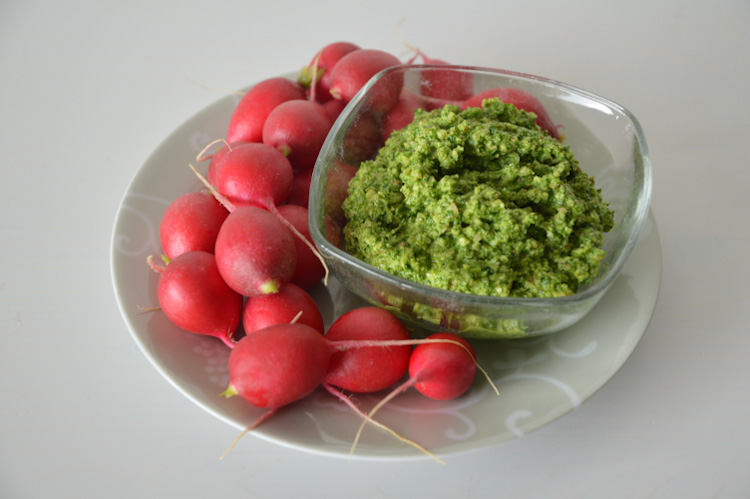 A white plate with bright pink radishes on one side and a bowl of bright green radish greens pesto on the other