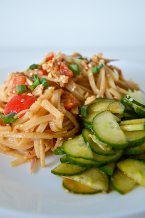 Close up of cold spicy sesame noodles with a side of cucumber salad, served on a white plate against a white background