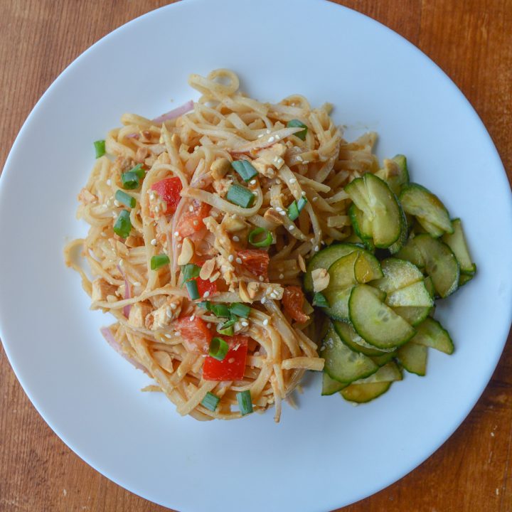 White plate of spicy peanut noodles, served cold, with cucumber salad