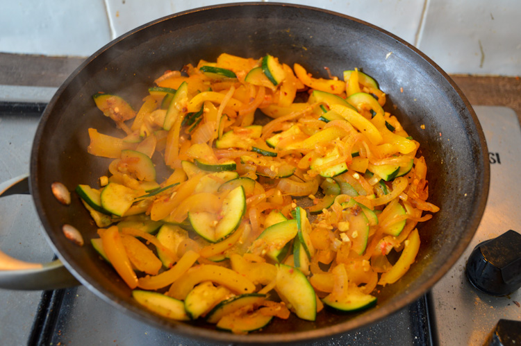 Vegetables sautéing in a skillet including yellow peppers and zucchini