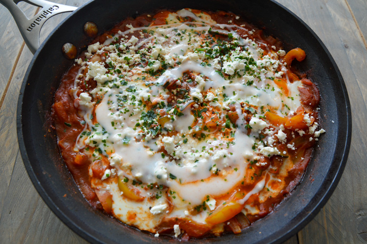 A skillet with shakshuka with feta, yogurt sauce, and parsley