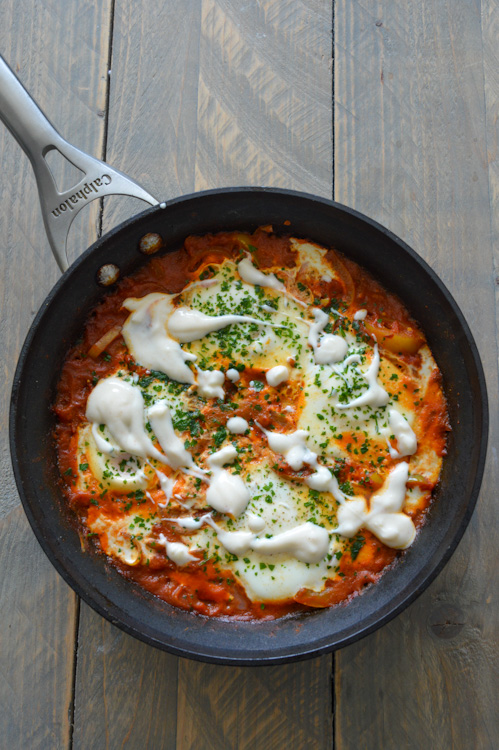 Shakshuka for two in a skillet with yogurt sauce and parsley on top