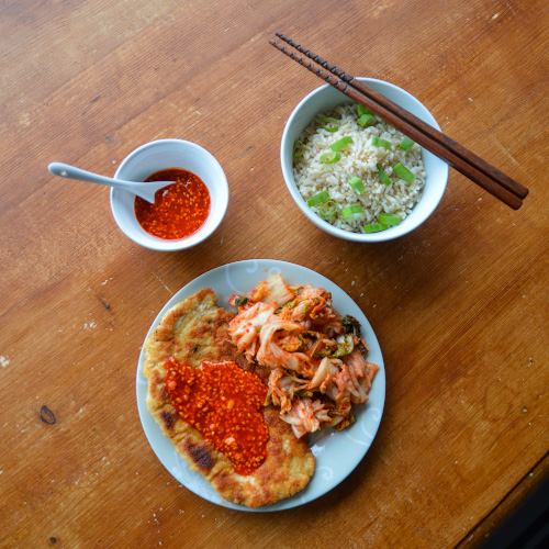 3 dishes on a brown table: small bowl of gochujang sauce, slightly larger bowl of rice with chopsticks, plate of Korean tonkatsu with kimchi