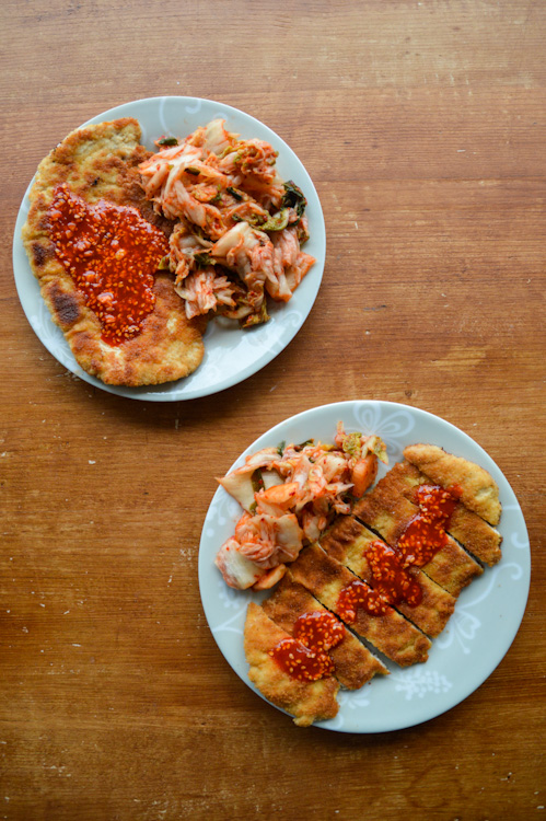 Two plates of Korean tonkatsu with gochujang sauce served with sides of kimchi