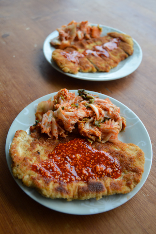 Two plates of Korean tonkatsu with gochujang sauce and kimchi, one clear in the foreground, one a bit blurred in the background