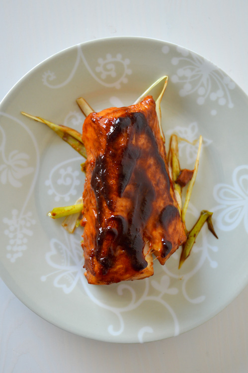 Top down view of one piece of baked cod fillet on a bed of julienned green onions; cod is topped with a miso ginger marinade glaze