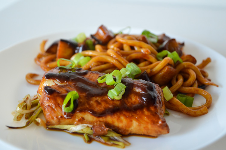 Side view of a plate of baked cod with miso ginger marinade and udon noodles topped with chopped green onions