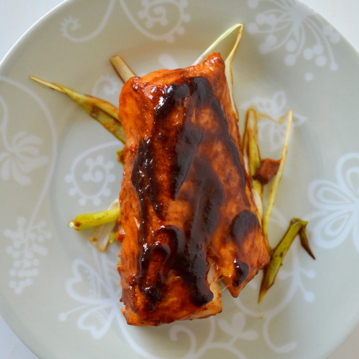 Baked cod with miso ginger marinade on a bed of scallions on a small plate