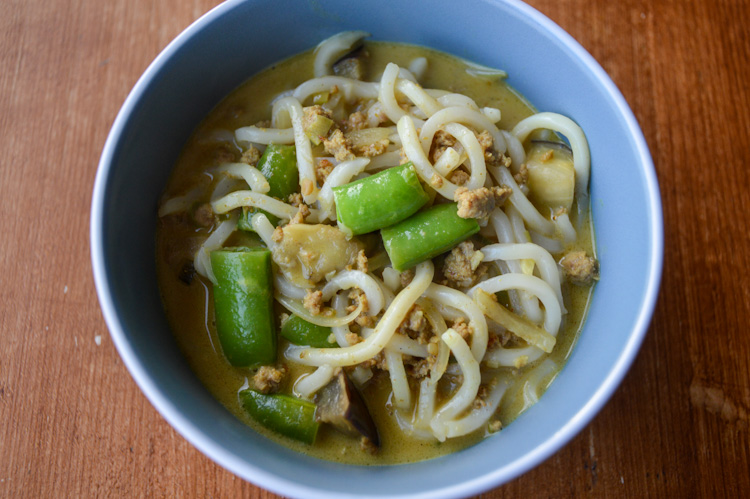 Close up of a blue bowl of curry udon with khao soi flavor with eggplant and sugar snap peas