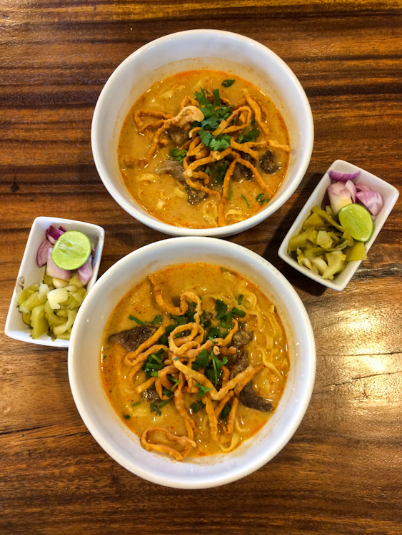 Overhead view of two bowls of khao soi with side dishes