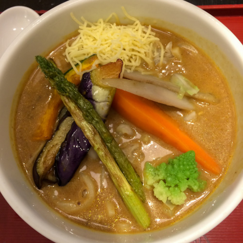 Bowl of Japanese curry udon with roasted vegetables and shredded cheese