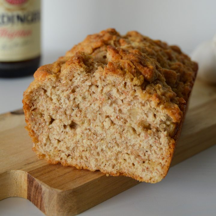 Loaf of whole wheat beer bread on a board with a beer in the background