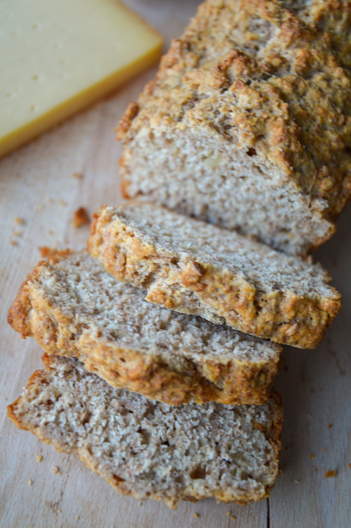 Sliced loaf of whole wheat beer bread on a wood board with a piece of cheese in the background