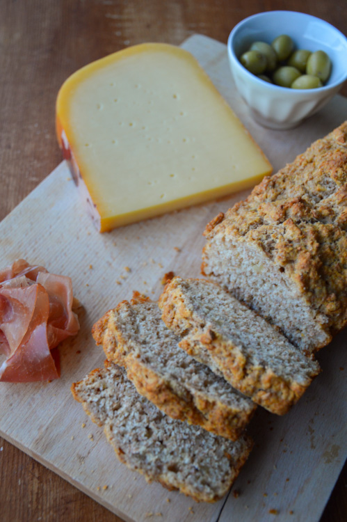 Wood board with sliced ham, cheese, olives, and a sliced loaf of beer bread