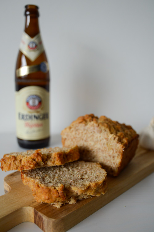 Half a loaf of beer bread on a small wood board in front of a bottle of wheat beer