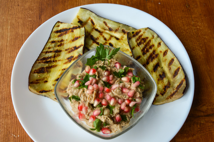 Eggplant pkhali in a bowl on a plate with three pieces of grilled eggplant