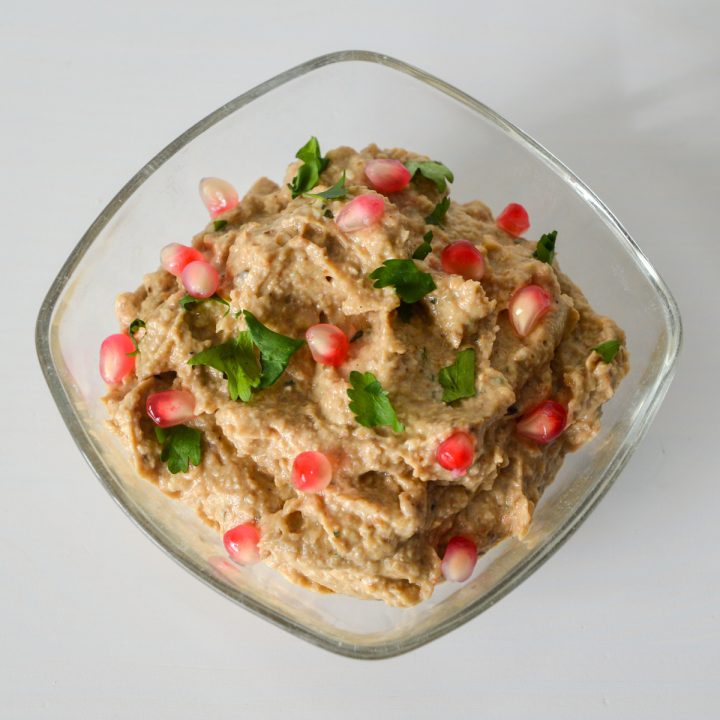 Eggplant pkhali in a glass bowl topped with pomegranate seeds and fresh green herbs