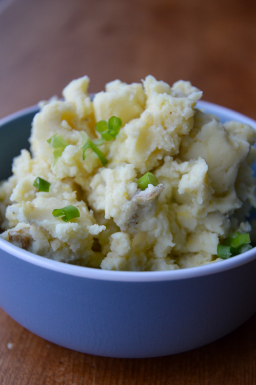 Miso mashed potatoes piled high (and topped with green onions) in a blue bowl on a wood table