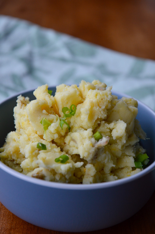 Blue bowl full of mashed potatoes with miso on a table with a green fabric in the background