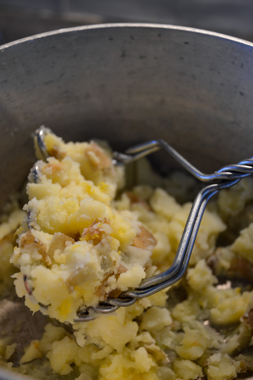 Miso mashed potatoes in the process of being mashed in a pot with a metal potato masher