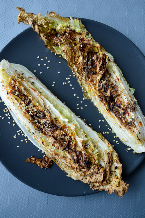 Two wedges of roasted napa cabbage topped with sesame seeds on a black plate