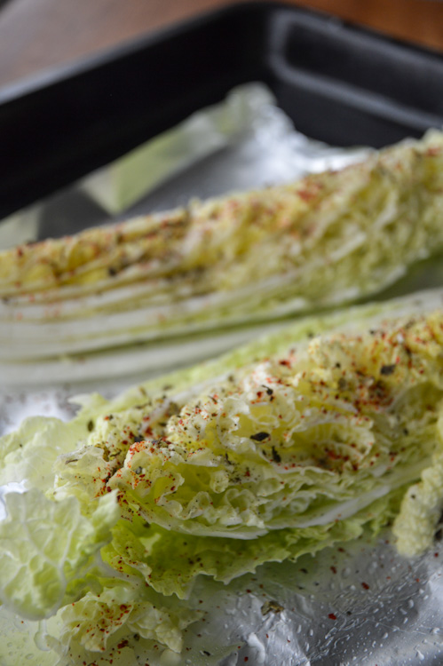 Two pieces of cabbage (one in focus, one blurry) with Sichuan peppercorns and chili flake being prepped to be roasted