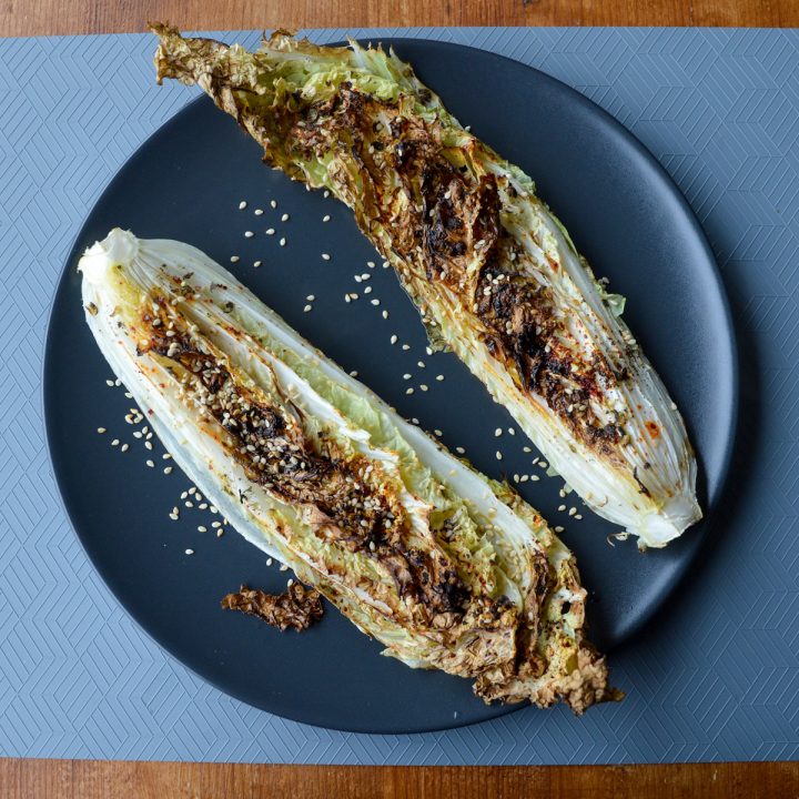 Roasted napa cabbage on a black plate sprinkled with sesame seeds